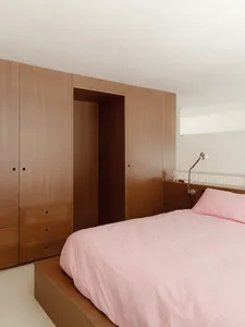 A cozy bedroom with a large bed, pink blanket, nightstands, and a dresser, creating a warm and relaxing atmosphere