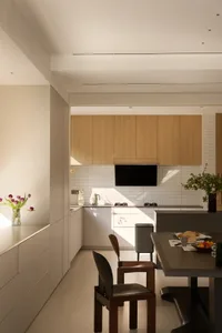 A modern kitchen and dining area with white walls and cabinets, featuring a dining table, chairs, TV, and decorative items, with a focus on functionality and aesthetics