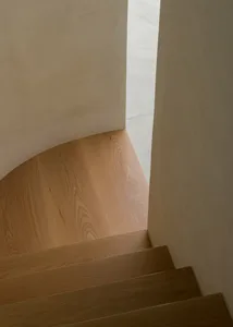 A curved staircase with a wooden handrail in a well-lit interior space with a warm atmosphere
