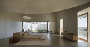 Open living area with a large bed, two chairs, a sink, and a refrigerator, surrounded by white walls and giving off a modern and minimalist vibe