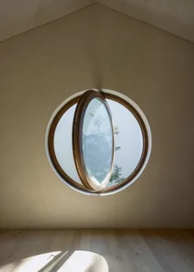 A modern room with a round window made of wood and glass, surrounded by white walls and wooden elements