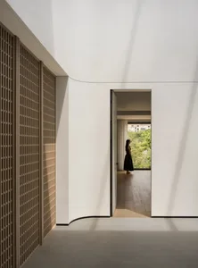 A woman stands near a doorway in a calm and peaceful hallway made of wood with a natural ambiance