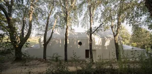 A rendered image of a white building with a circular window, surrounded by trees in a suburban or semi-rural area