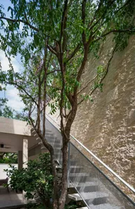 A modern staircase with metal steps and a brick wall in the background, with a tree in front and a second-story balcony above
