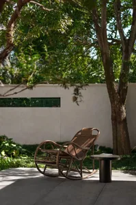 A wicker chair sits on a concrete surface in front of a tree, with two books nearby, creating a relaxing outdoor seating area
