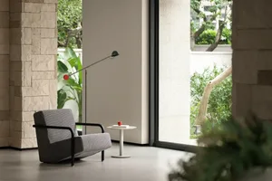 A gray chair sits in front of a window in a calm and inviting living space with natural light and two potted plants nearby