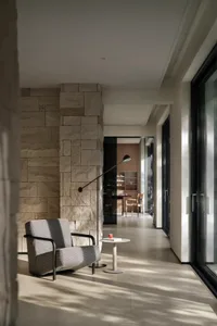 A cozy living room with a grey chair near a stone wall, two dining tables, and a decorative vase