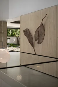 A modern room with a wall featuring two large wooden leaf sculptures, accompanied by three potted plants placed near the left, center, and right sides of the wall
