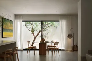 Cozy dining space with a wooden table, three chairs, and a potted plant, surrounded by natural light