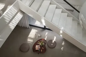 Bright open living area with a white staircase, two couches, a dining table, and a potted plant, surrounded by ample seating options