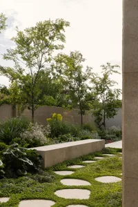 A serene outdoor garden area with a stone bench in front of a brick wall, surrounded by trees
