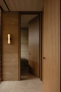 A warm and inviting hallway with wooden features, lit by a single light source, revealing a room beyond two open doors