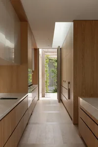 A warm and inviting kitchen and hallway area with wooden floors and cabinets, featuring two sinks and a doorway leading to the outside