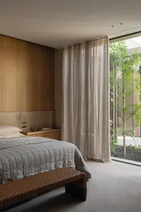Cozy bedroom with wooden walls and floors, featuring two beds, a chair, and a large window allowing natural light to enter