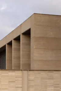 A modern building with a large concrete wall featuring two arches, set against a daylight background