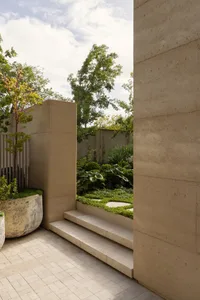 A serene outdoor garden area with a concrete wall, staircase, and lush greenery, featuring potted plants and a harmonious balance between nature and architecture
