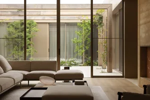 Open modern living area with wooden walls, two couches, a chair, and a dining table, flooded with natural light from large windows