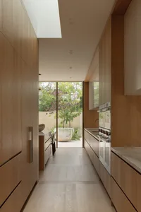 Open kitchen with wooden cabinets and flooring, featuring two sinks, a refrigerator, oven, utensils, and a bowl, in a clean and well-organized atmosphere