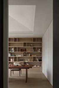 A cozy living area with a wooden bookshelf filled with books, vases, and a chair for reading or relaxation