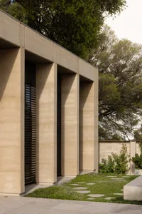 A modern building facade with three large concrete pillars supporting the structure, showcasing a minimalist design with a sense of depth and contrast from the lighting