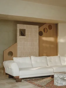 Coastal living room with a white couch, brick-patterned wall, two chairs, and a bird perched on the couch, creating a warm and inviting atmosphere