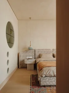 A simple bedroom with two beds and nightstands on a wooden floor, beige walls, and a minimalistic design