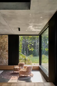Cozy living space with a black interior design theme, a couch in front of a large window overlooking a garden, and two chairs placed throughout the room