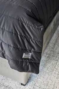 A dimly lit bedroom with a gray comforter on a bed, creating a cozy atmosphere