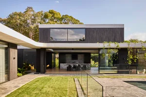Open modern living area with a large kitchen, dining table, and living room, featuring white walls, black accents, and natural light from several windows