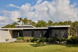 Modern house with a black exterior, grassy yard, and natural light from windows, surrounded by trees