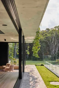 A modern house with a glass door leading to a well-lit patio area with two chairs, surrounded by a comfortable and inviting living space