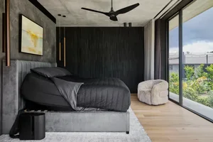 A modern bedroom with a black bed on a wooden floor, gray and white tones, ceiling fans, a chair, and a potted plant