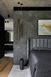 A modern bedroom with a metal bed, gray walls, and a couch, lit by lamps on either side of the bed
