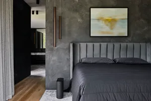 A modern bedroom with a black bed in front of a large picture, grey walls, two lamps, and a potted plant adding greenery