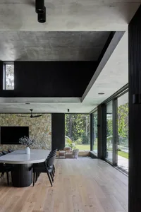 Open living area with a large table, potted plants, TV, and modern design elements including wood flooring, stone walls, and glass doors