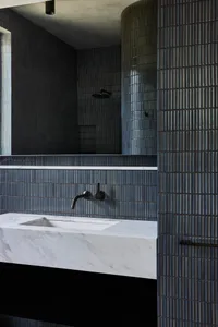 Double sink bathroom with marble countertop, tile wall, and shower, reflected in a mirror
