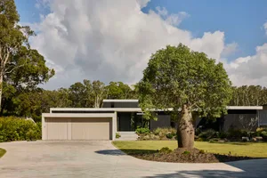 A black house with a garage and potted plants surrounded by trees and greenery in a suburban setting