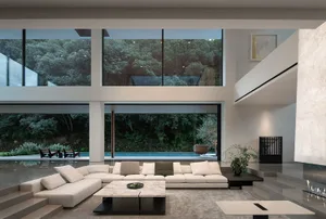 Open modern living area with a white couch, glass wall, chairs, and dining table, giving off a clean and minimalist vibe