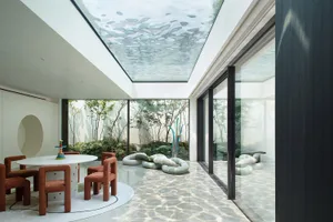 Open modern living area with a glass ceiling, white walls, and floors, featuring chairs, a dining table, and two couches