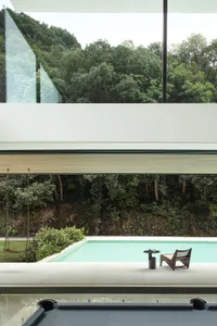 Indoor pool area with a large glass wall offering a view of the surrounding forest, two chairs, and an empty pool