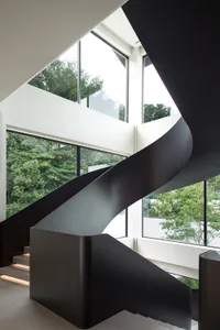 A modern staircase with black railings and metal steps, set against white walls and natural light from multiple windows