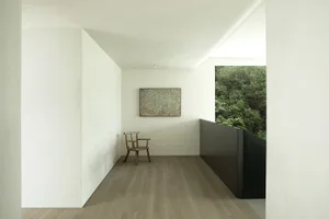 Calm and inviting living space with white walls, wooden floors, a chair, a painting, and two windows