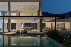 A modern indoor swimming pool area with a glass enclosure, surrounded by chairs and dining tables, creating a relaxing and inviting atmosphere