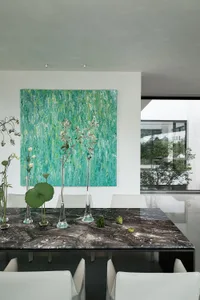A cozy dining space with a table, chairs, vases with flowers, potted plants, and a painting on the wall