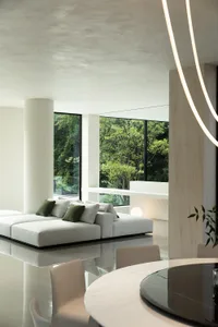 A modern living room with white walls and floors, featuring two couches, two chairs, and a potted plant, with a bright and open feel