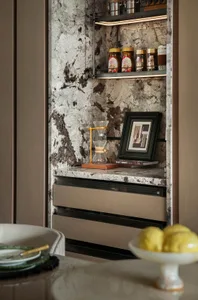 Elegant kitchen with a marble countertop featuring two clocks, three bottles, and a vase, creating a sophisticated atmosphere