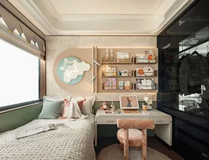 Cozy bedroom with a white bed, wooden desk, and chair in front of a window, with a teddy bear and books on a bookshelf