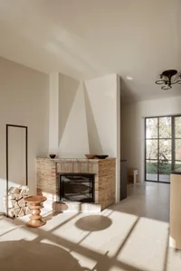 Cozy living room with a brick fireplace, a couch, a chair, and a dining table, featuring white walls and warm lighting