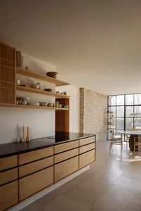 Warm kitchen with wooden cabinets, black countertops, and white walls, featuring a dining table and chairs, and decorative vases and bowls