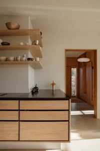 Modern kitchen with wooden cabinets, a black countertop, and a white wall, featuring several bowls on the countertop in a well-lit space